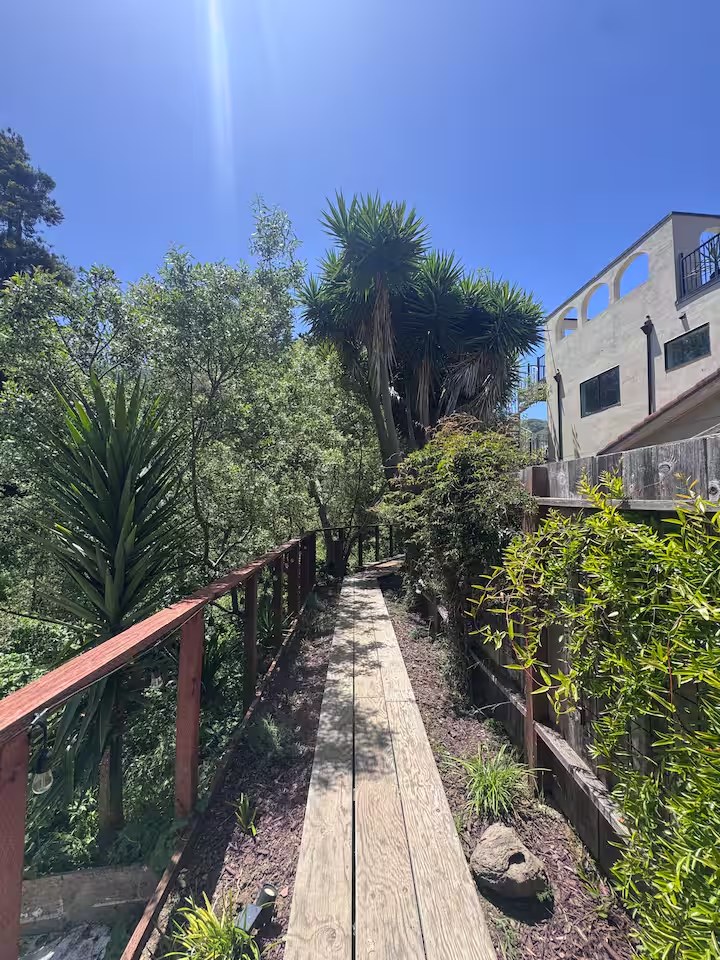 Private wooden walkway lined with lush tropical plants and a wooden railing leading toward the house